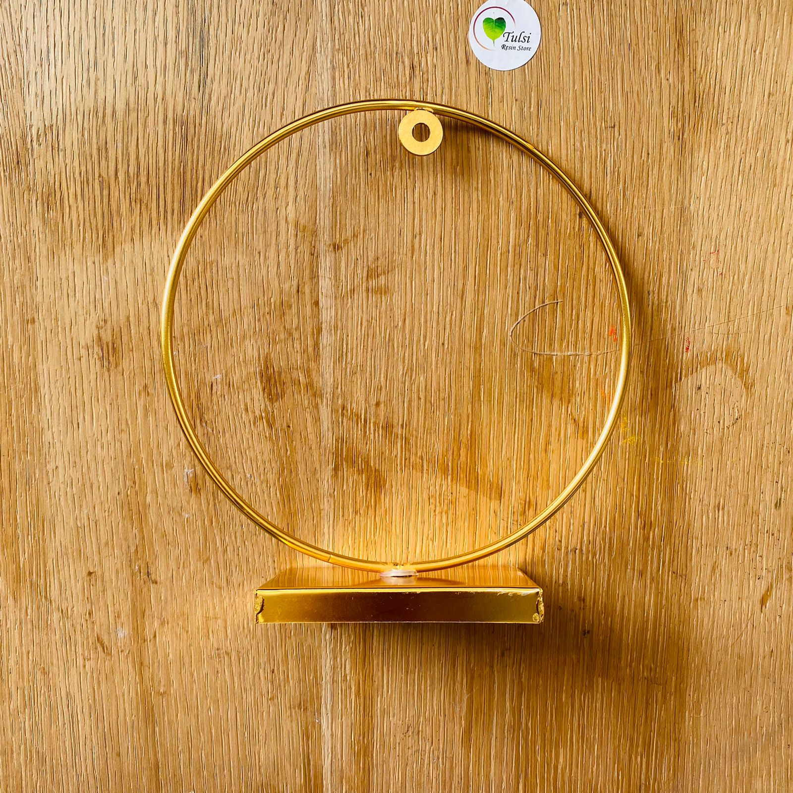 A golden metal loop stand with a round base and a circular hoop, placed on a wooden surface.